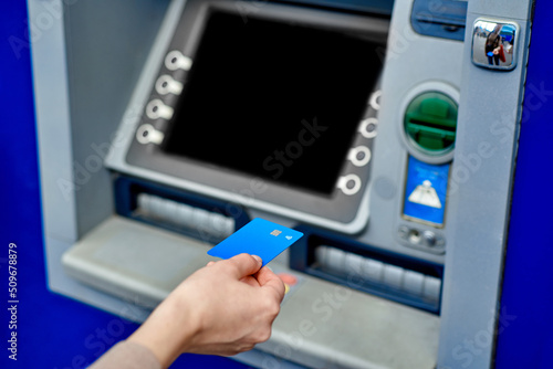 The girl's hand inserts the bank card into the ATM. Blue bank card. A woman uses an ATM on the street.