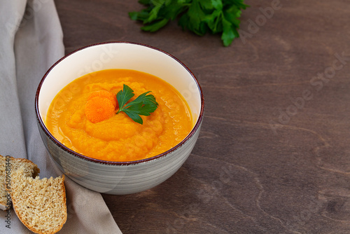 carrot cream soup with fresh carrots and herbs on wooden background. Carrot soup with parsley on brown table. Spring vegetable soup. Homemade cream soup with copy space.