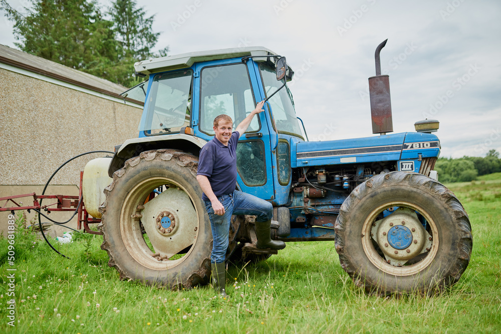 Come take a look in my office. Portrait of a cheerful young farmer posing next to his large farm tractor outside on a field. Come take a look in my office. Portrait of a cheerful young farmer posing next to his large farm tractor outside on a field.
