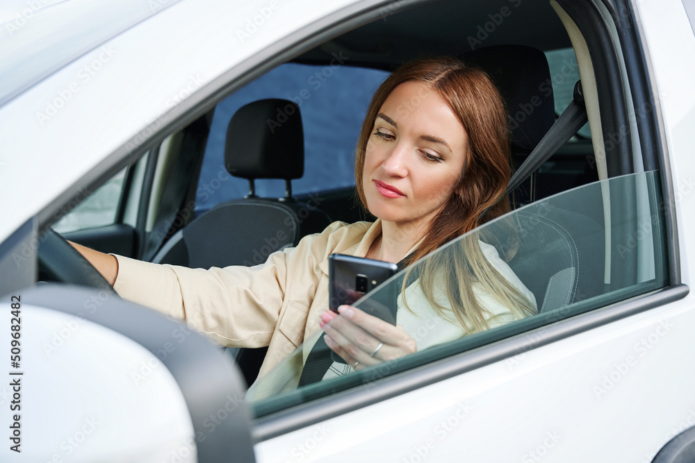 Woman is looking on the phone while driving a car. The concept of danger on the road and inattentive car driving