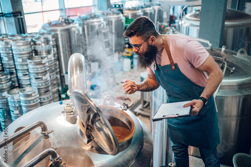 Canvas Print Man working in brewery and taking notes of the beer production