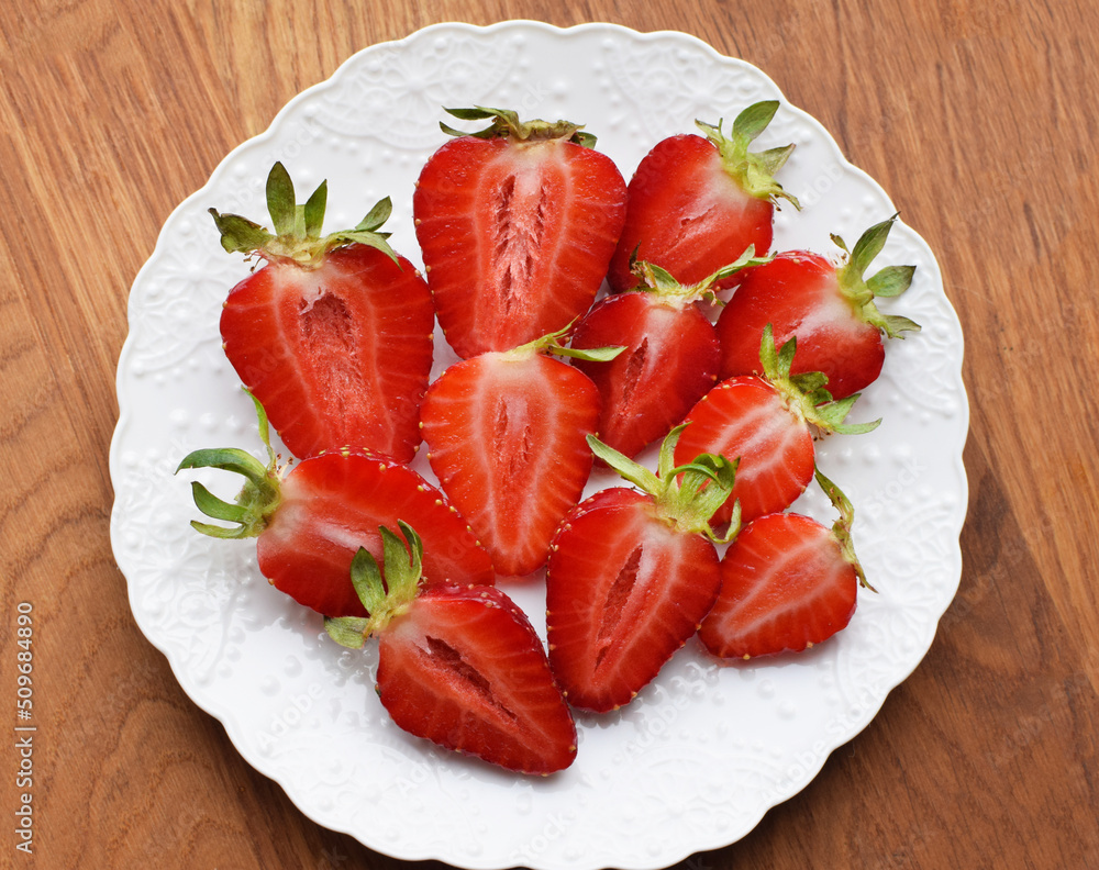 Ripe juicy strawberries cut in halves on a white plate. Ripe juicy strawberries cut in halves on a white plate.