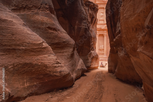 Al Siq Canyon in Petra, Jordan, pink red sandstone walls both sides, unrecognizable person sitting on camel distance, Treasury temple behind