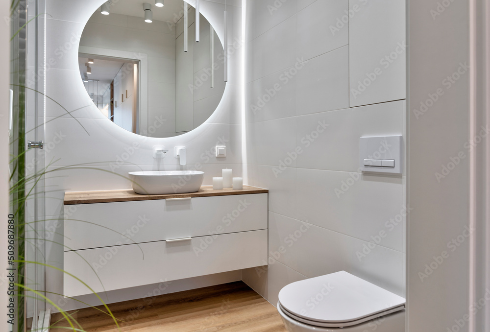 Interior of bathroom with ceramic bowl on the wooden cabinet, wooden tile on the floor, round mirror with led lights. Stylish bathroom with wc and bath. - obrazy, fototapety, plakaty 