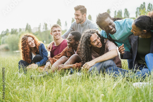 Multiracial happy people having fun sitting on grass outdoor - Soft focus on man with long hair