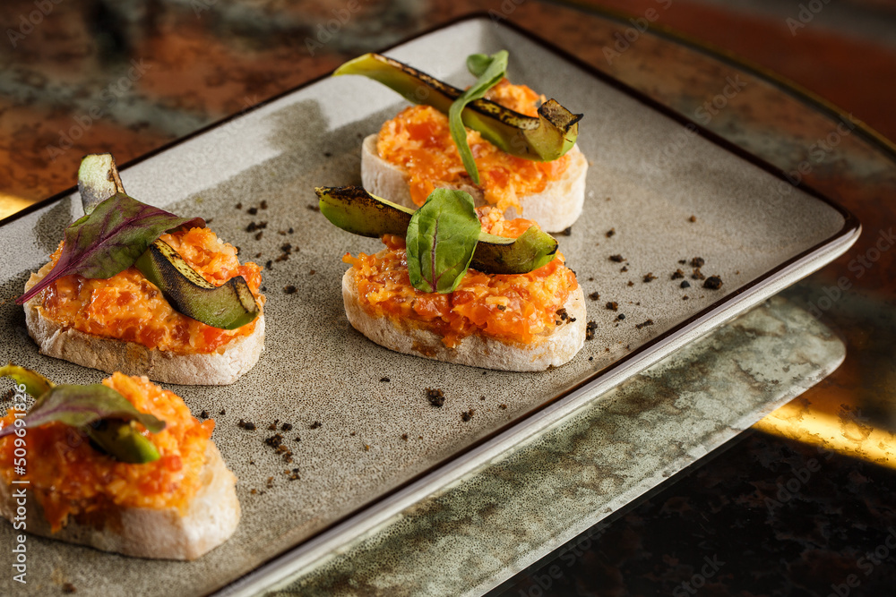 baked bruschetta with salmon, cheese, sun-dried tomatoes and avocado in gray plate on bright background