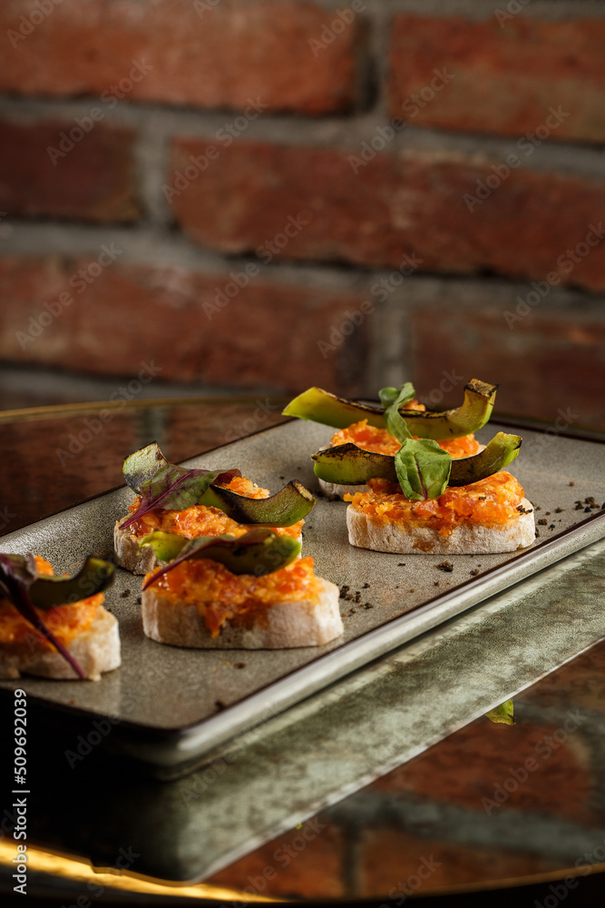 baked bruschetta with salmon, cheese, sun-dried tomatoes and avocado in gray plate on bright background