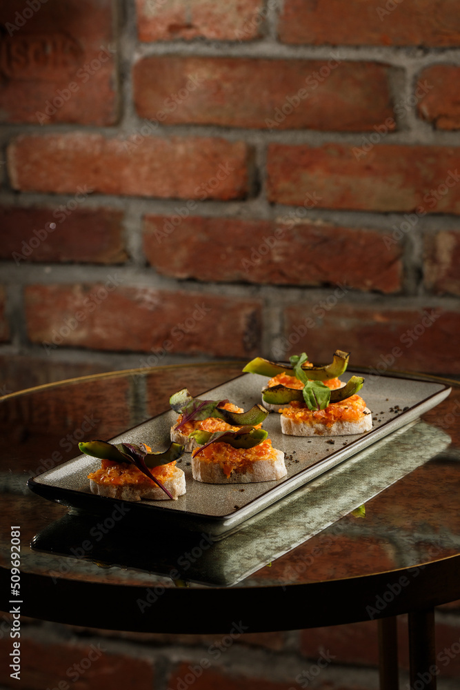 baked bruschetta with salmon, cheese, sun-dried tomatoes and avocado in gray plate on bright background