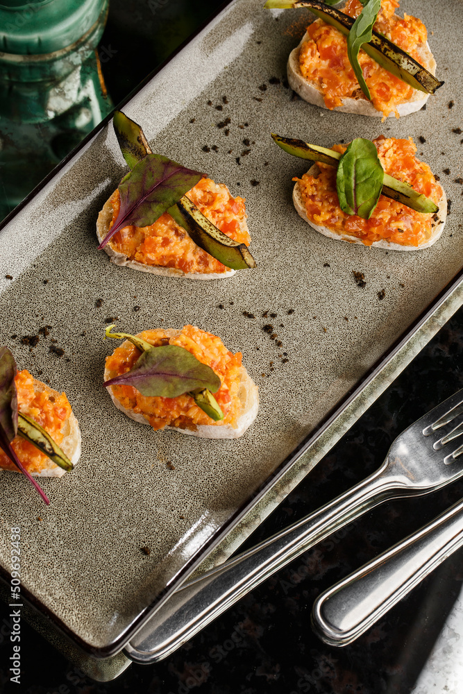 baked bruschetta with salmon, cheese, sun-dried tomatoes and avocado in gray plate on bright background