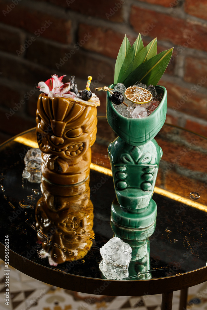 Tiki Drink Cocktails. Two cocktails in different glasses against the background of a bar decorated with dried fruits and tropical leaves.