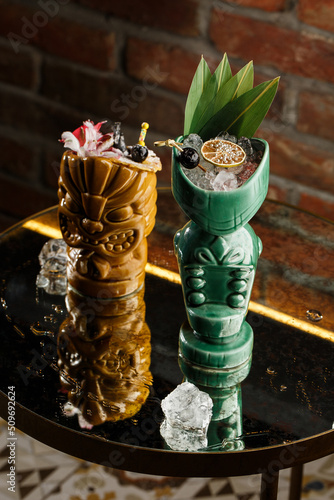 Obraz na płótnie Tiki Drink Cocktails. Two cocktails in different glasses against the background of a bar decorated with dried fruits and tropical leaves. w salonie