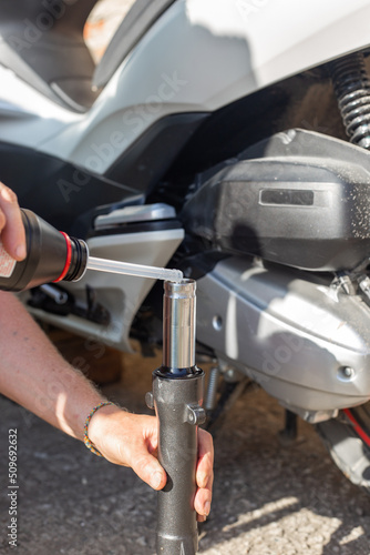 A car mechanic repairs a motorbike. A man pours oil into the shock absorber of the front fork of a scooter