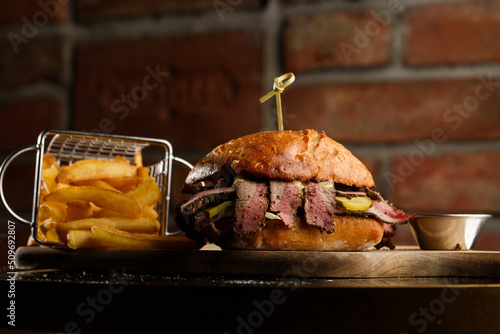 Obraz na płótnie Pastrami sandwich on rye bread served with pickles and mustard sauce. Tasty sandwich with french fries potatoes on dark background. w salonie