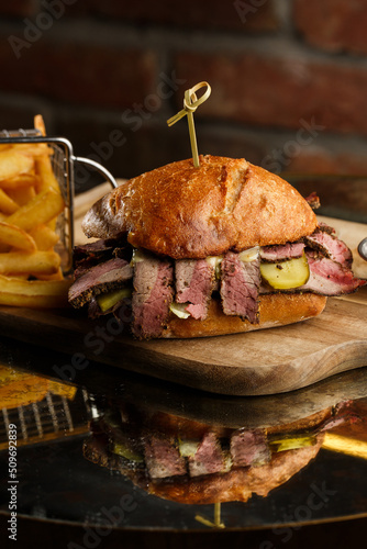 Obraz na płótnie Pastrami sandwich on rye bread served with pickles and mustard sauce. Tasty sandwich with french fries potatoes on dark background. w salonie
