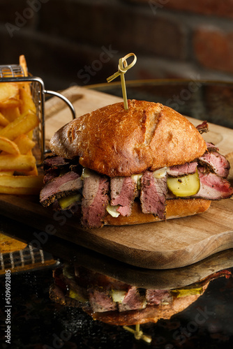 Obraz na płótnie Pastrami sandwich on rye bread served with pickles and mustard sauce. Tasty sandwich with french fries potatoes on dark background. w salonie