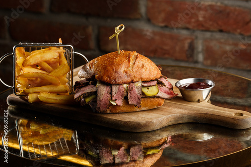 Obraz na płótnie Pastrami sandwich on rye bread served with pickles and mustard sauce. Tasty sandwich with french fries potatoes on dark background. w salonie