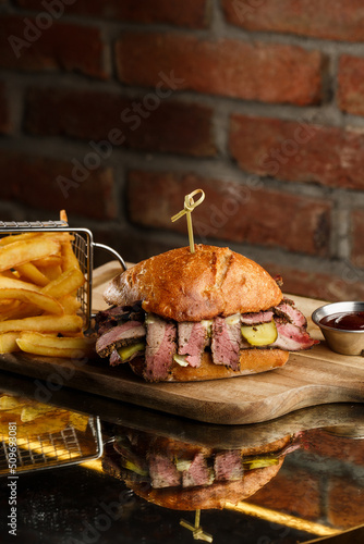 Obraz na płótnie Pastrami sandwich on rye bread served with pickles and mustard sauce. Tasty sandwich with french fries potatoes on dark background. w salonie