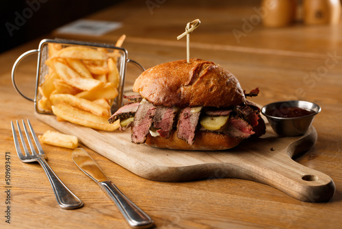 Obraz na płótnie Pastrami sandwich on rye bread served with pickles and mustard sauce. Tasty sandwich with french fries potatoes on dark background. w salonie
