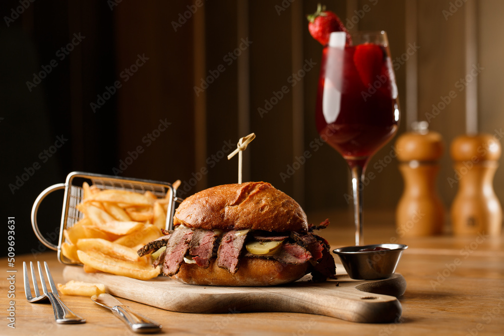 Pastrami sandwich on rye bread served with pickles and mustard sauce. Tasty sandwich with french fries potatoes and Sangria drink on dark background.