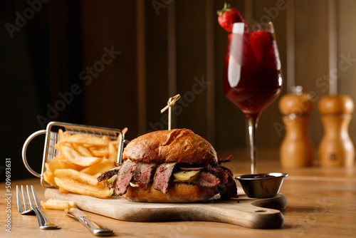 Obraz na płótnie Pastrami sandwich on rye bread served with pickles and mustard sauce. Tasty sandwich with french fries potatoes and Sangria drink on dark background. w salonie
