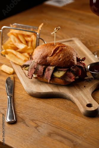Obraz na płótnie Pastrami sandwich on rye bread served with pickles and mustard sauce. Tasty sandwich with french fries potatoes on dark background. w salonie