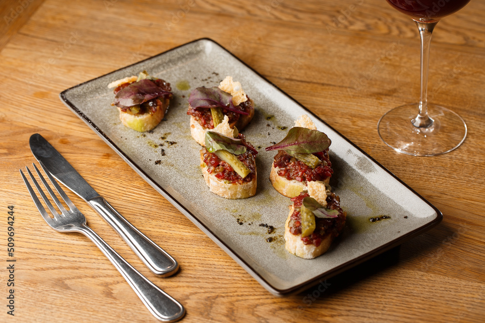 Four bruschettas with beef tartare on a plate, Crostini with Beef Tartare, beef Bruschetta, sandwich with raw gourmet beef.