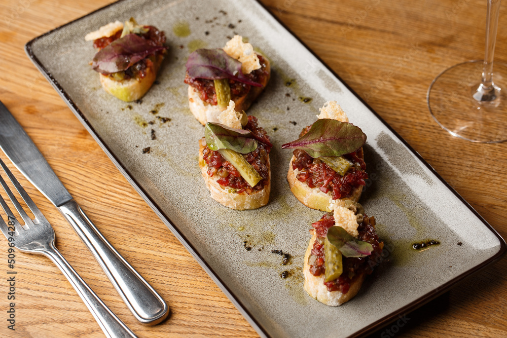 Four bruschettas with beef tartare on a plate, Crostini with Beef Tartare, beef Bruschetta, sandwich with raw gourmet beef.