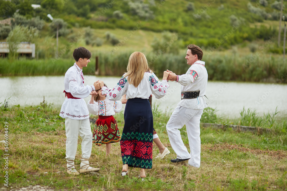 Fototapeta premium Happy family with kids in traditional romanian clothes dancing outside.