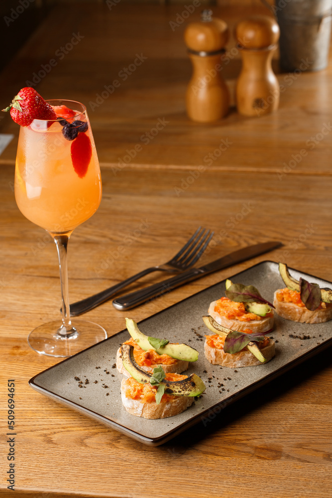 baked bruschetta with salmon, cheese, sun-dried tomatoes and avocado in gray plate on bright background