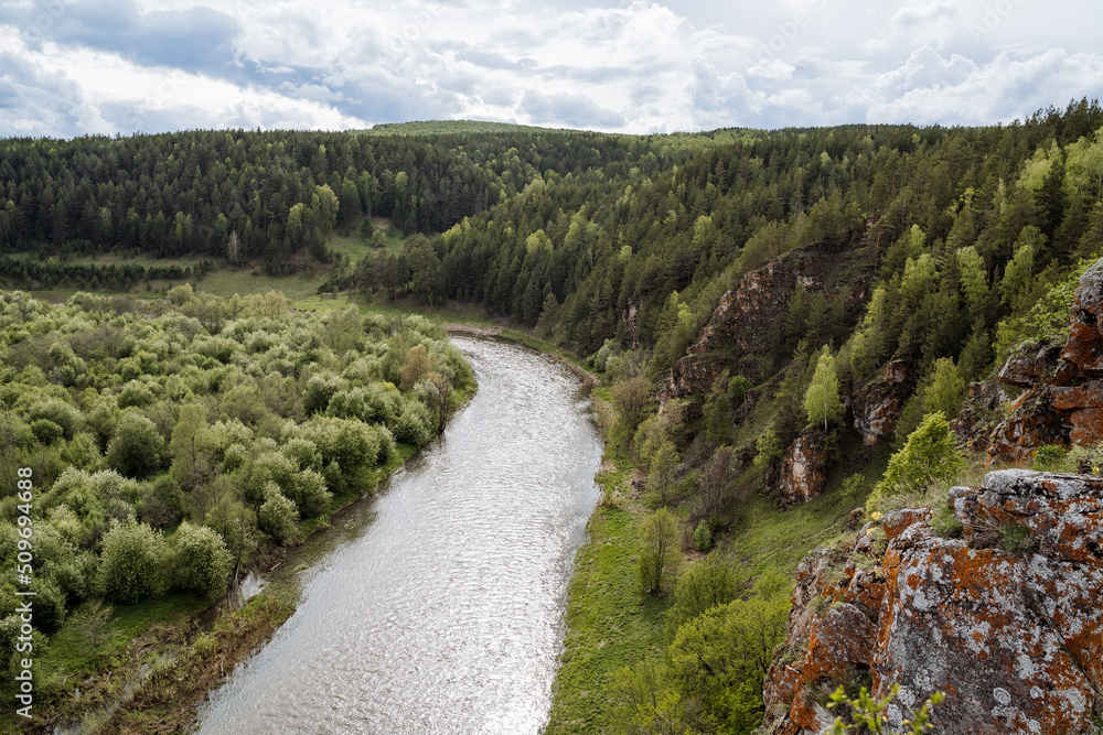 The nature of Russia, the taiga area, the reserved land, the landscape of the mountain river, the orange rock against the background of the green forest, the overcast sky.