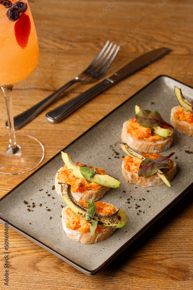 baked bruschetta with salmon, cheese, sun-dried tomatoes and avocado in gray plate on bright background