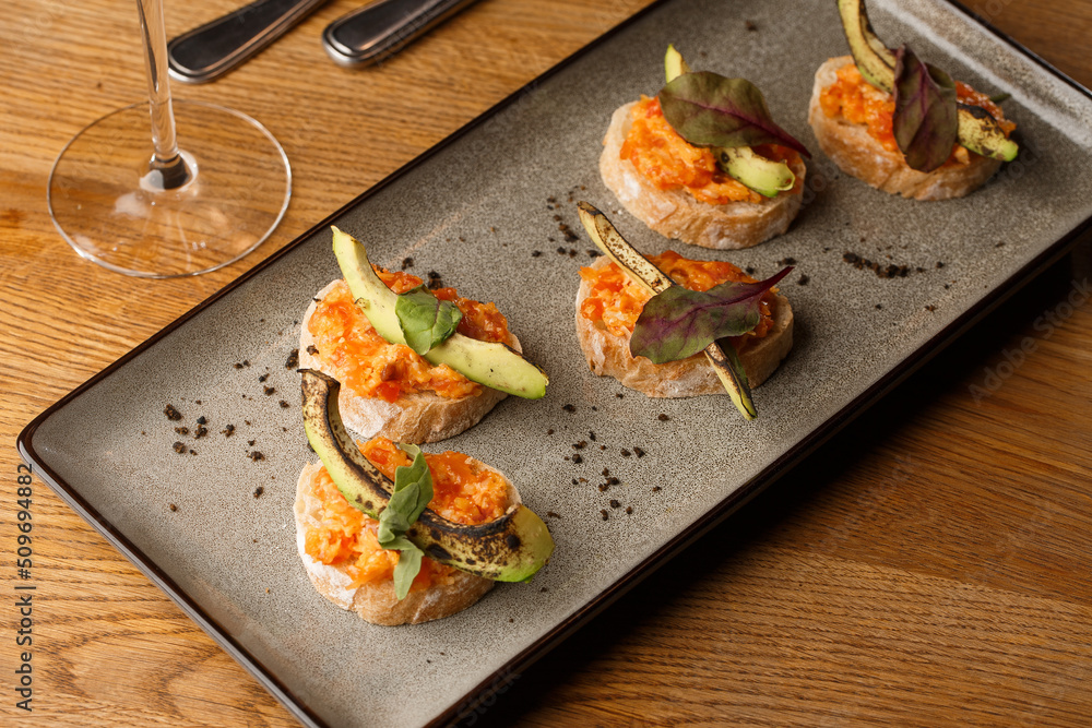 baked bruschetta with salmon, cheese, sun-dried tomatoes and avocado in gray plate on bright background