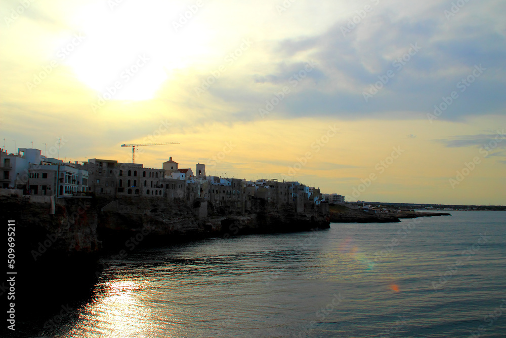 Gorgeous rocky coast in Polignano a Mare full of Apulian houses washed by the peaceful Adriatic sea with water surface reflecting golden light of the evening sun