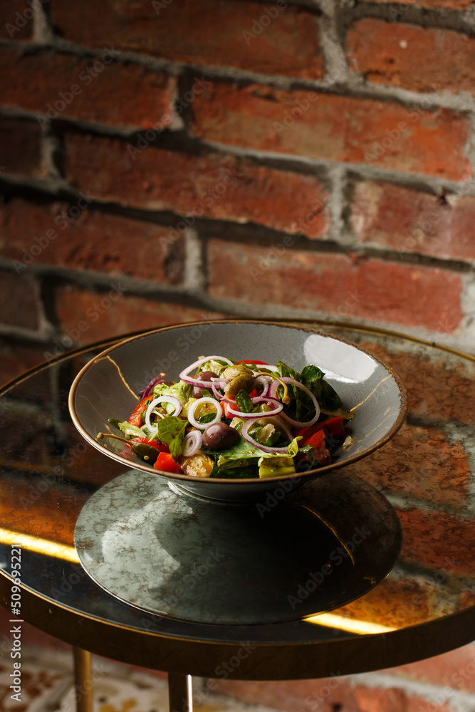 Greek salad with fresh vegetables: tomato, cucumber, red bel pepper, lettuce, onion, olives and cheese. Close-up on a white round plate on a wooden background. Salad menu with ingredients