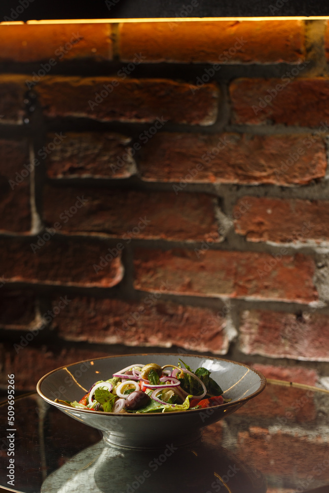 Greek salad with fresh vegetables: tomato, cucumber, red bel pepper, lettuce, onion, olives and cheese. Close-up on a white round plate on a wooden background. Salad menu with ingredients