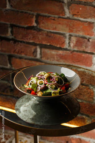 Obraz na płótnie Greek salad with fresh vegetables: tomato, cucumber, red bel pepper, lettuce, onion, olives and cheese. Close-up on a white round plate on a wooden background. Salad menu with ingredients w salonie