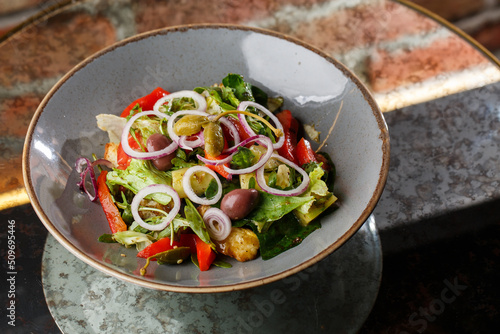 Obraz na płótnie Greek salad with fresh vegetables: tomato, cucumber, red bel pepper, lettuce, onion, olives and cheese. Close-up on a white round plate on a wooden background. Salad menu with ingredients w salonie