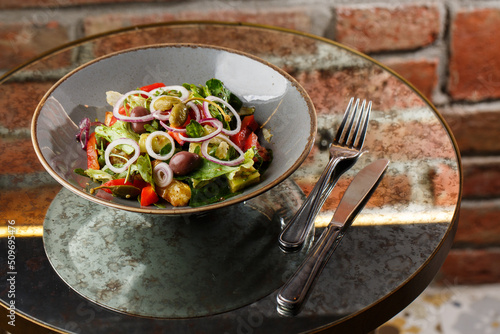 Obraz na płótnie Greek salad with fresh vegetables: tomato, cucumber, red bel pepper, lettuce, onion, olives and cheese. Close-up on a white round plate on a wooden background. Salad menu with ingredients w salonie