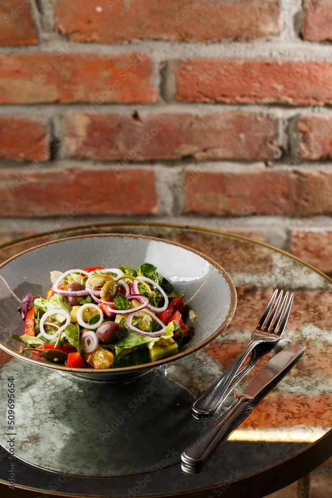 Greek salad with fresh vegetables: tomato, cucumber, red bel pepper, lettuce, onion, olives and cheese. Close-up on a white round plate on a wooden background. Salad menu with ingredients