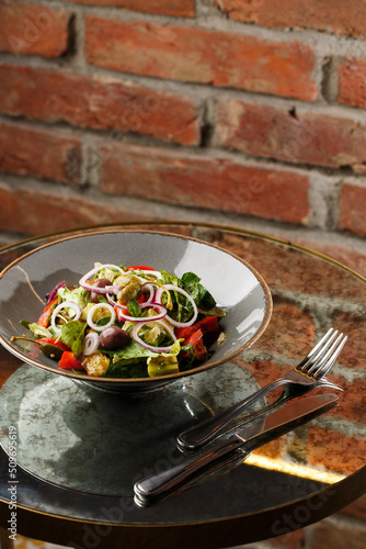 Obraz na płótnie Greek salad with fresh vegetables: tomato, cucumber, red bel pepper, lettuce, onion, olives and cheese. Close-up on a white round plate on a wooden background. Salad menu with ingredients w salonie