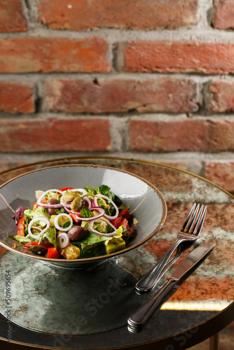 Obraz na płótnie Greek salad with fresh vegetables: tomato, cucumber, red bel pepper, lettuce, onion, olives and cheese. Close-up on a white round plate on a wooden background. Salad menu with ingredients w salonie