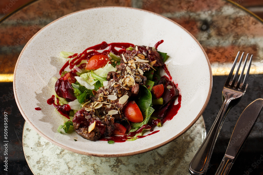 Salad with veal and tomatoes. Beef steak with raw vegetables mix side view. Grilled meat with garnish close-up. Delicious main course on table