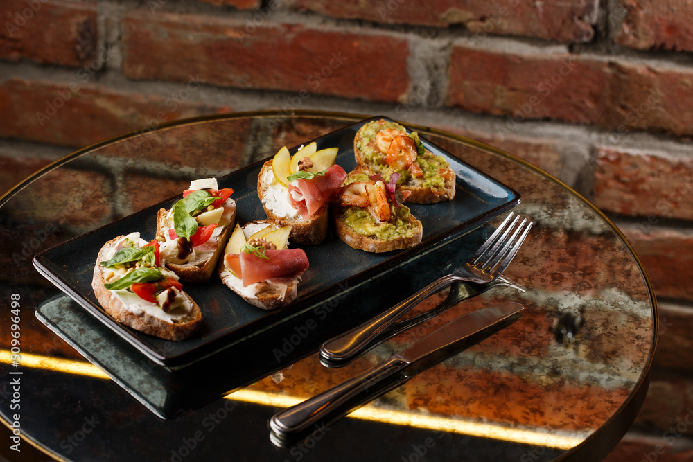 Bruschettas with vegetables. Start dishes with cherry tomatoes, avocado, cream cheese and shrimps. Food composition, tasty italian meal