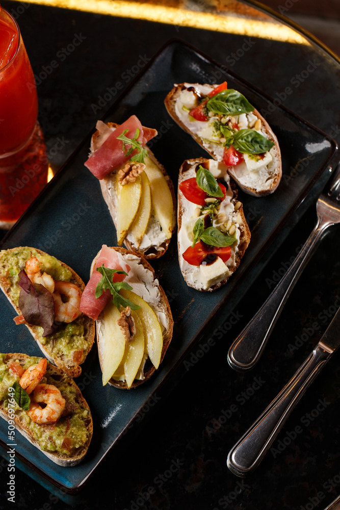 Bruschettas with vegetables. Start dishes with cherry tomatoes, avocado, cream cheese and shrimps. Food composition, tasty italian meal
