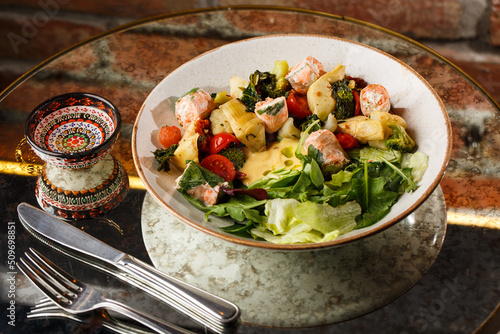 A salad with grilled salmon, mashed avocado and lettuce dressed with cream cheese. Close-up of the dish in a brown bowl isolated on brown background.