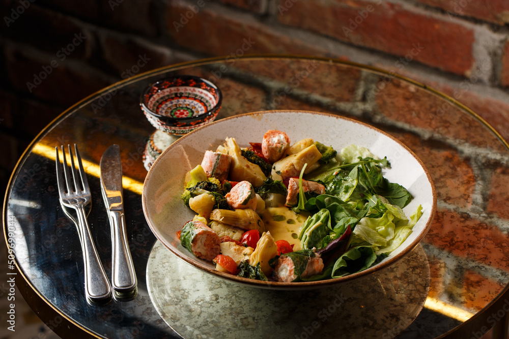 A salad with grilled salmon, mashed avocado and lettuce dressed with cream cheese. Close-up of the dish in a brown bowl isolated on brown background.