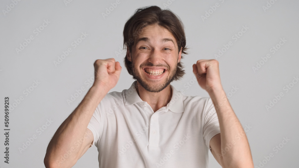Attractive man raising clenched fists celebrating success at camera feeling like winner over gray background. Winner expression Attractive man raising clenched fists celebrating success at camera feeling like winner over gray background. Winner expression