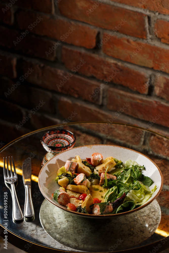 A salad with grilled salmon, mashed avocado and lettuce dressed with cream cheese. Close-up of the dish in a brown bowl isolated on brown background.