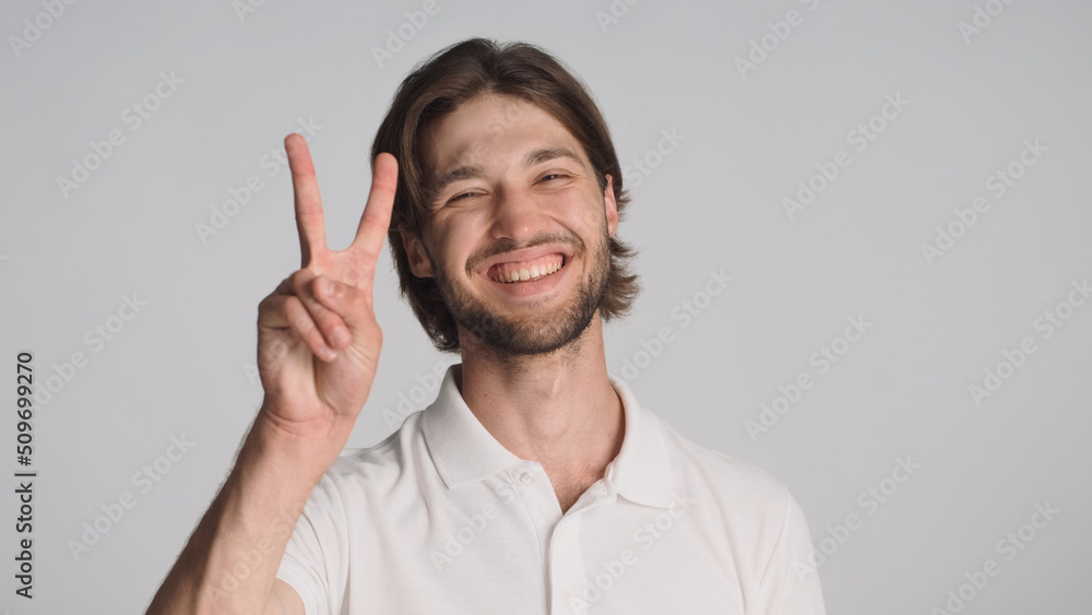 Cheerful guy showing peace sign sincerely smiling at camera over gray background. Young positive man posing in studio Cheerful guy showing peace sign sincerely smiling at camera over gray background. Young positive man posing in studio