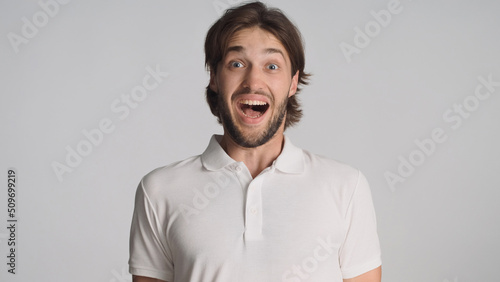 Surprised bearded guy looking excited at camera over white background. Attractive man with open mouth looking amazed